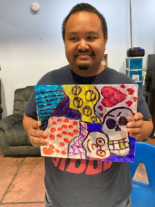 Participant showing colorful abstract marker artwork with lines, boxes, hearts, squiggles, and cartoon faces.