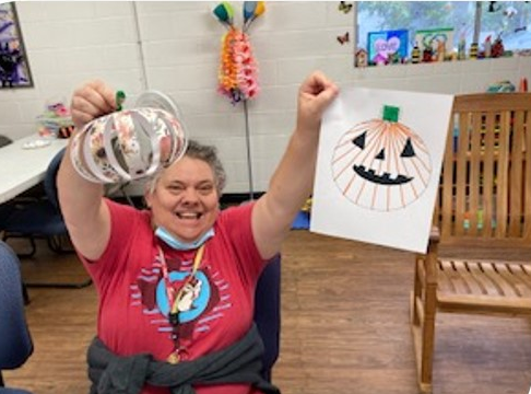 A smiling participants holding us a line-art pumpkin and a paper pumpkin sculpture.