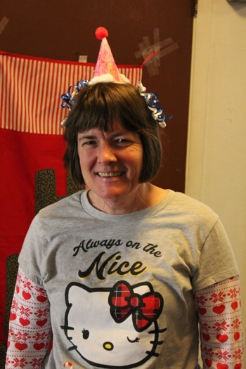 Smiling participant wearing a holiday fascinator made from a water cone, markers, pom poms, cord, and ribbon.