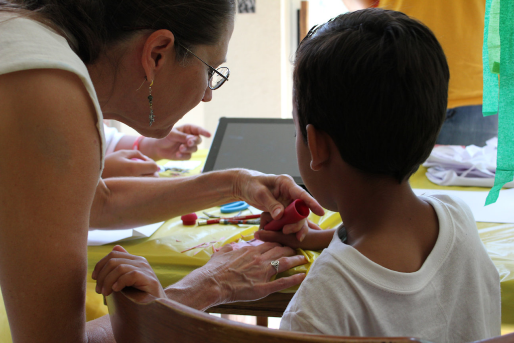 Back view of adult showing a child how to use a print cutting tool.