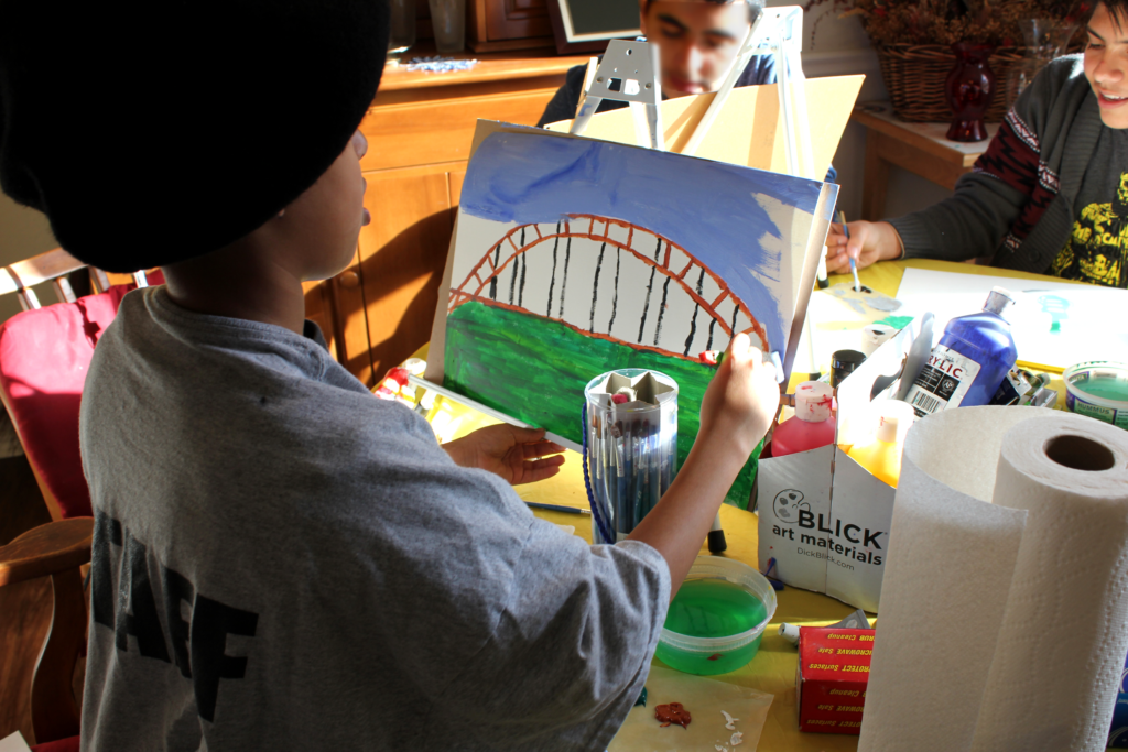 Back view of child wearing a black beret and creating an acrylic painting of the Pennybacker Bridge.