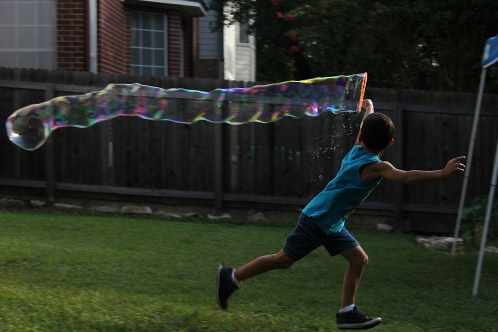 Child in shirt and shorts trailing a huge bubble behind him as he runs.