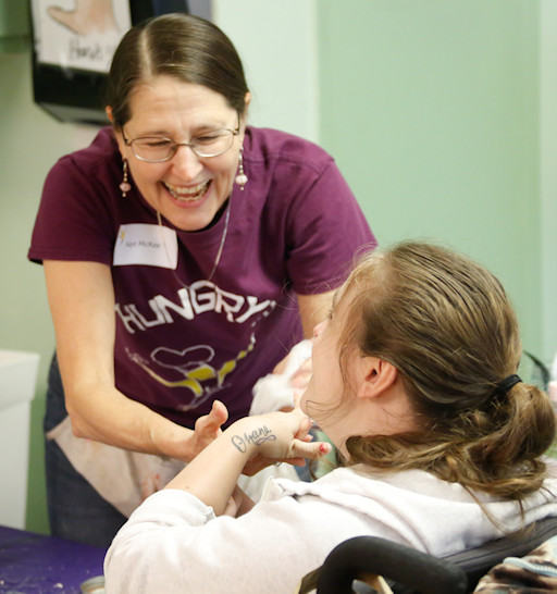 Kaye in a purple A Spacious Place Tee shirt assisting a student with a smile.