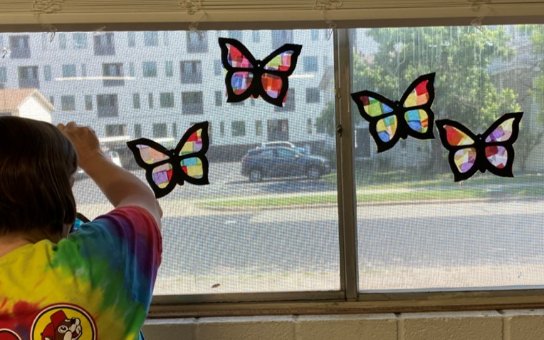 Student hanging colorful butterfly suncatchers in a window.