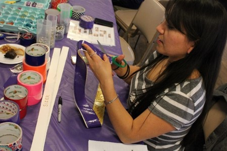 Participant is using scissors to cut purple and gold duct-tape for a duct-tape belt activity.