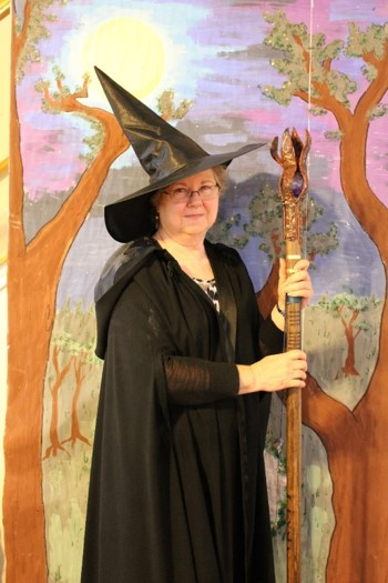 Participant dressed in black robe and wizard hat with wizard staff in from of a woodland backdrop posing for holiday card.