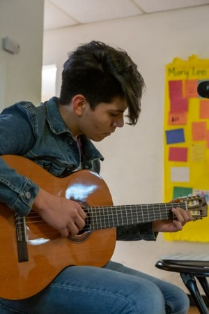 Young musician seated and playing guitar for Gifted2Give.